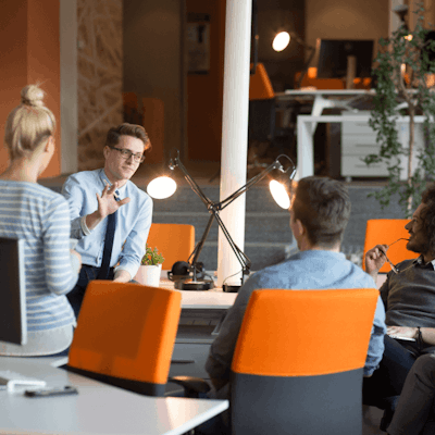 Ein Team von Fachleuten, die in einem modernen Büro mit orangefarbenen Stühlen und Schreibtischlampen diskutieren.